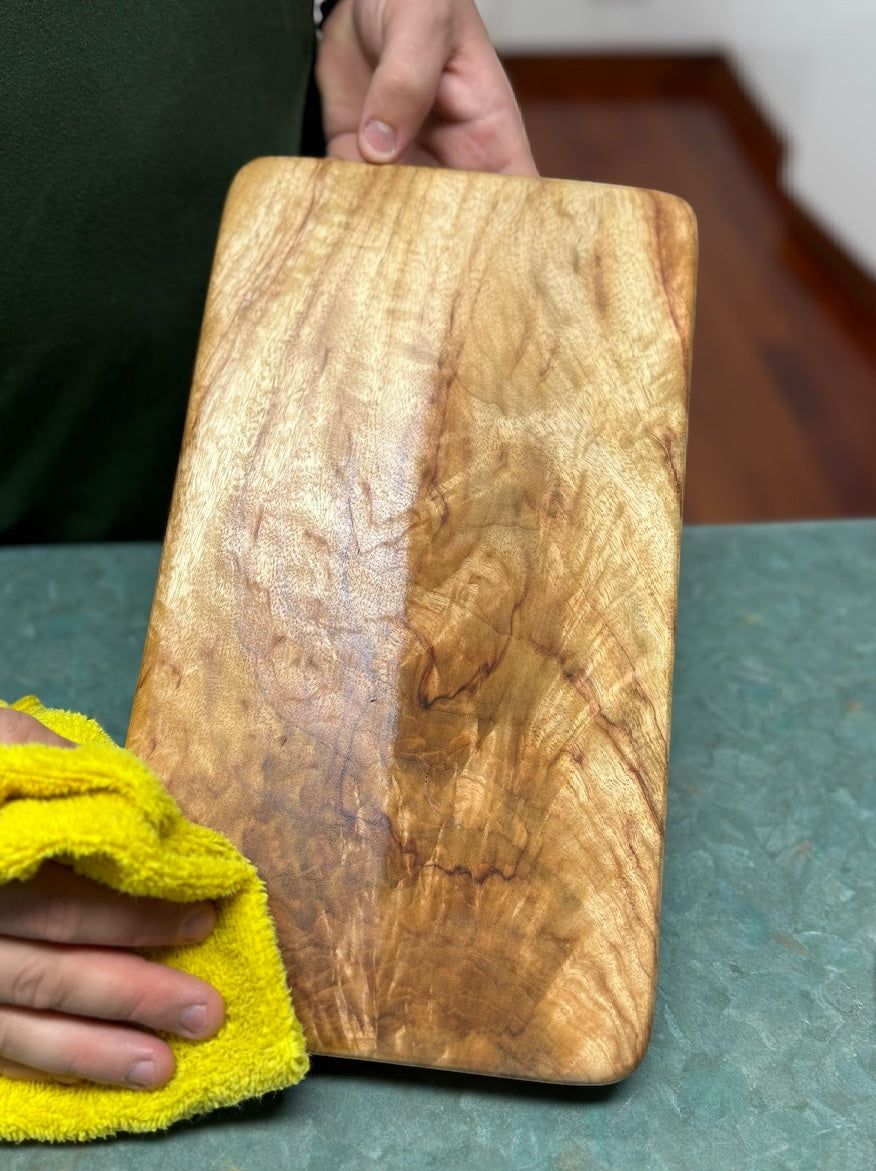 Think4Earth Tung Oil and Liquid Beeswax set nourishing a wooden cutting board. The oil enhances the wood grain.