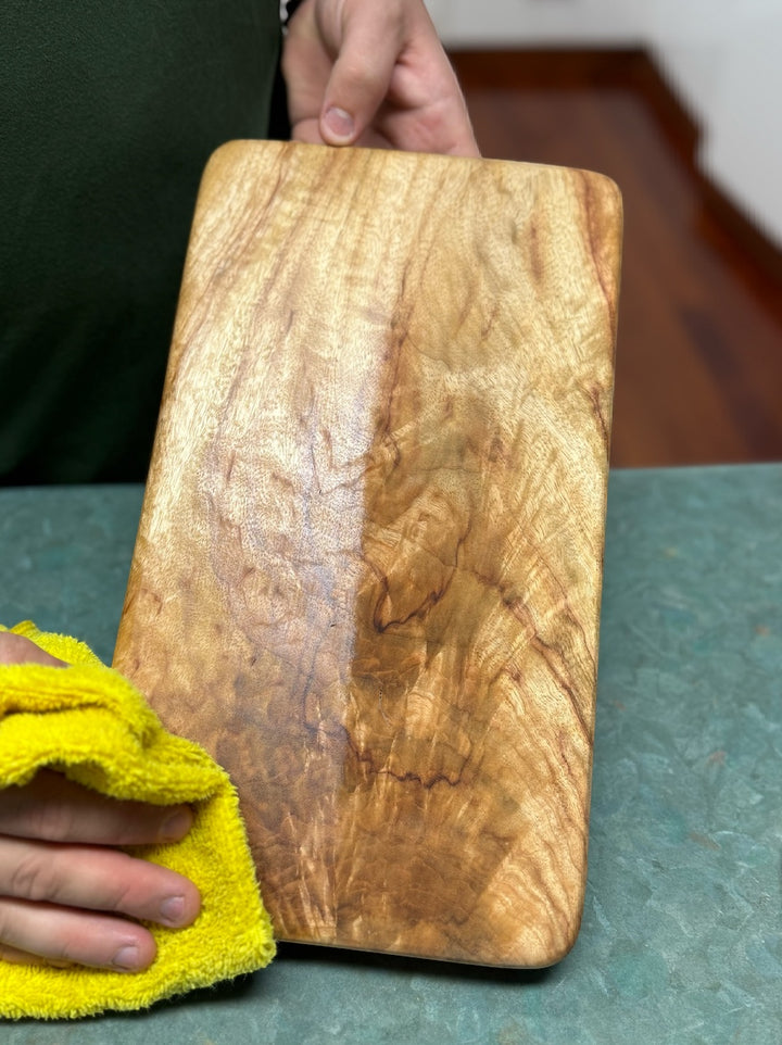 Think4Earth Tung Oil and Liquid Beeswax set nourishing a wooden cutting board. The oil enhances the wood grain.